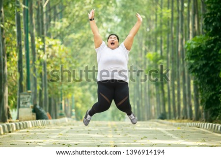 Picture of excited fat woman wearing sportswear while jumping on the road