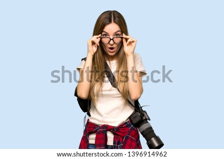 Young photographer woman with glasses and surprised on isolated blue background