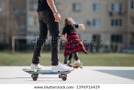 Young father and his son dressed in the stylish casual clothes rides skateboards on a platform outside next to the house at the sunny warm day