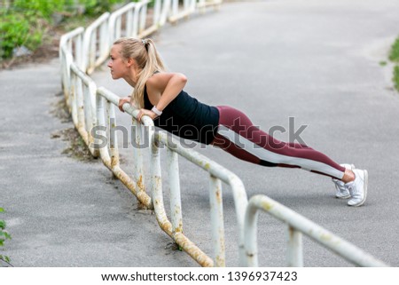 Fitness lifestyle. Young woman doing push ups in the slope. Sporty young blonde girl on a sunny day at the stadium. Healthy life concept. Horizontal photo.