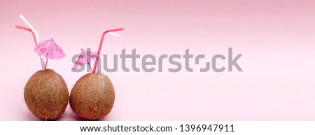 Coconut with drinking straw and umbrella on pink background.