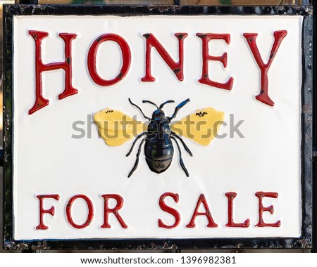 Honey for sale sign with a bee as symbol - red lettering and white background