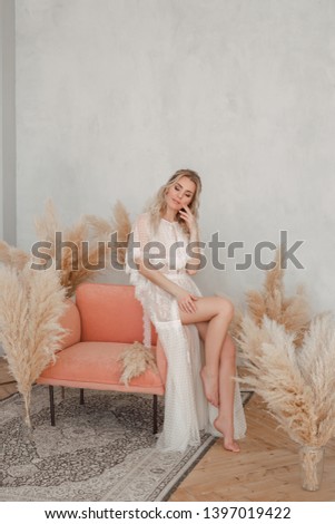 The beautiful girl with a fair hair in a white dress sits on an armchair