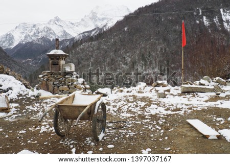 Valley is covered with snow. Scene is Mountains, Stone pile,red flag,Construction cart,small pagoda. It's cliff in Aden village, 
Yading Nature Reserve, China. It's beautiful places on Tibetan Plateau