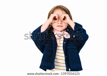 Little brunette girl is looking through hands, formed in binocular like fashion. Pretty dressed.