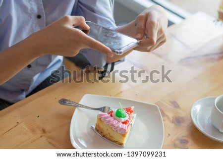 hand of female taking picture of strawberry cake with her smartphone at cafe and bakery