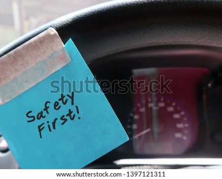 A blue paper note sticking on the car steering wheel, with text written SAFETY FIRST, to remind the driver to drive carefully and avoid distraction while on the road. Royalty-Free Stock Photo #1397121311