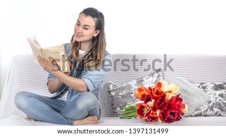 Young girl reading a book on the couch in the living room , next to a large bouquet of tulips .
