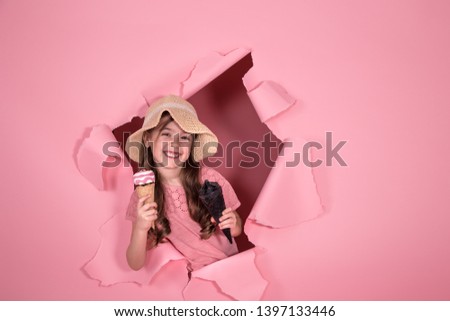 funny little girl peeking out of the hole in a beach hat and ice cream in her hands, on a colored pink background, space for text, Studio shooting