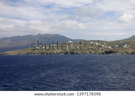 Photo of Tinos island as seen from distance on a stormy day with deep blue sea and cloudy sky, Cyclades, Greece