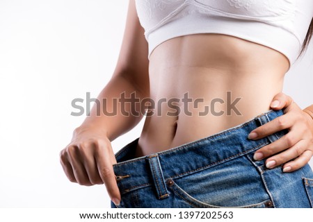 Young slim woman in oversized blue jeans. Fit woman wearing too large pants. Healthcare and woman diet lifestyle concept to reduce belly and shape up healthy stomach muscle. Royalty-Free Stock Photo #1397202563