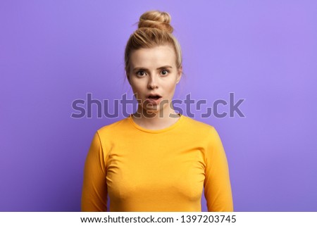 emotional charming stylish scared girl with opened mouth looking at the camera, isolated over blue background. close up portrait