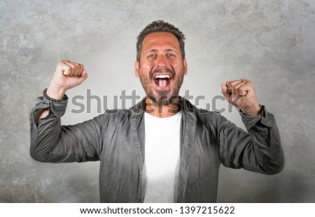 portrait of young happy and attractive Caucasian man gesturing with fist raising arms in victory and success sign smiling cheerful excited feeling strong emotion isolated on studio background