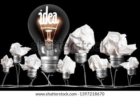 Large group of crumbled paper light bulbs and shining one of them with fiber in IDEA shape isolated on black background; concept of Idea, Innovation and Standing out