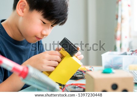 Closeup: Smart looking Asian boy working with circuits, wires, computer chip, OLED, motor, wheels on his robotics project. Science, Technology, Engineering and Mathematics (STEM) education concept. Royalty-Free Stock Photo #1397230448