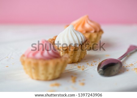 Small cakes with cream on a white table with a spoon. Selective focus. Front view.
