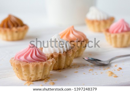 Small cakes with cream on a white table with a spoon and a mug. Selective focus. Front view.