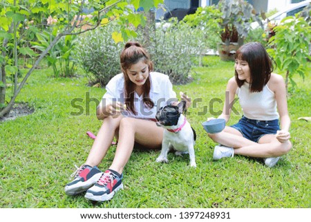 beautiful two young asian woman wearing white shirt who sitting on grass and playing with her cute dog with happy and smiling face in garden with green trees. (friendship concept)