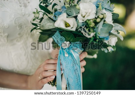 bouquet of wedding flowers with blue ribbons in the hands of the bride