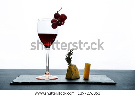 Glass of red wine garnished with grape and pieces of savory cheese.