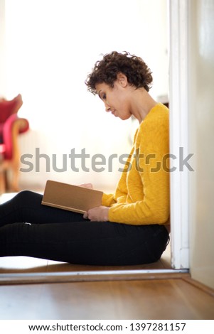 Side portrait of young african american woman sitting on floor with book