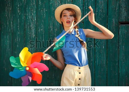Young happy funny (vintage) dressed woman with colorful weather vane,looking like flower. Old green fence on the background.  Picture ideal for illustating woman magazines.
