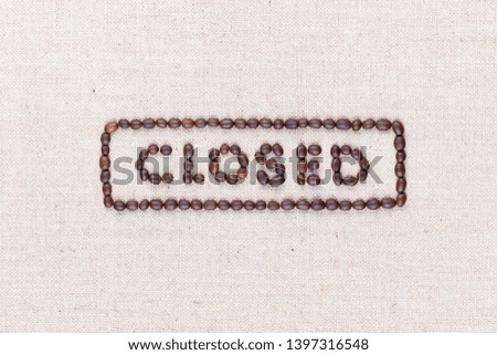 The word Closed inside a rectangle written with coffee beans on creamy linea canvas, shot from above, aligned in the center,closeup.