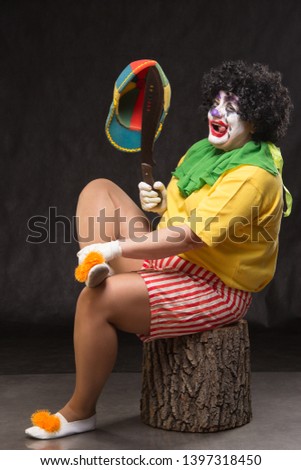 Scary clown with a horrible make-up laughs and with big knives in hands on a black background