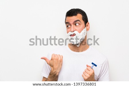 Man shaving his beard over isolated white background unhappy and pointing to the side