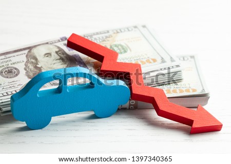 Red arrow graphics down on the background of the car and a stack of money cash dollars. Concept of falling car market, insurance, lower prices, repair costs