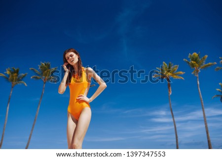 A woman in a yellow swimsuit, high palms blue sky summer heat tropics                      