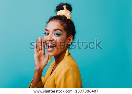 Refined black girl wears yellow earrings chilling during photoshoot. Studio portrait of joyful african lady with blue makeup.