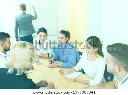 Group of smiling students brainstorming in classroom while man student writing on whiteboard