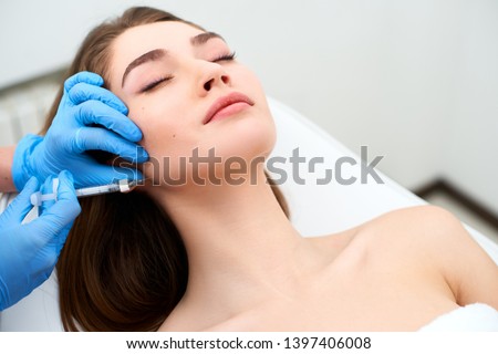 Beautician doctor with filler syringe making injection to jowls. Masseter lines reduction and face contouring therapy. Anti-aging treatment and face lift in cosmetology clinic. Patient lying on chair Royalty-Free Stock Photo #1397406008