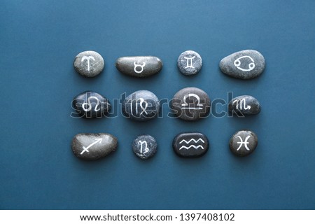 Stones with painted Zodiac signs on color background
