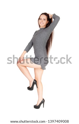 A beautiful slim young woman standing with one leg up in a gray
dress, smiling and dancing, isolated for white background
