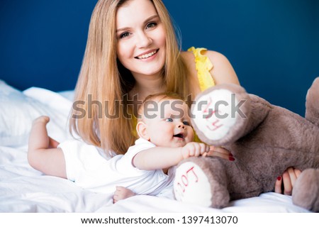Smiling mom and infant girl kid playing with teddy bear in bedroom