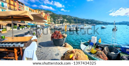 Panoramic cityscape with street cafe and fishing boat  in resort town Villefranche sur Mer. Cote d'Azur, France     Royalty-Free Stock Photo #1397434325