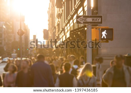 Sunlight shines on the busy crowds of anonymous people walking down the street in Midtown Manhattan, New York City NYC