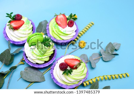 cupcakes with whipped cream decorated chocolate bar, strawberry ,macaroons on blue background. Picture for a menu or a confectionery catalog. with space for text. decorated with eucalyptus leaves.