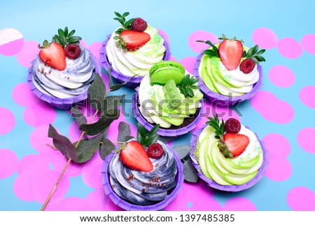 cupcakes with whipped cream decorated chocolate bar, strawberry ,macaroons on blue background. Picture for a menu or a confectionery catalog. with space for text. decorated with pink confetti.