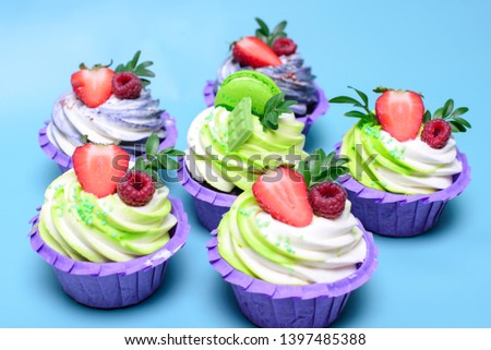 cupcakes with whipped cream decorated chocolate bar, strawberry ,macaroons on blue background. Picture for a menu or a confectionery catalog. with space for text.