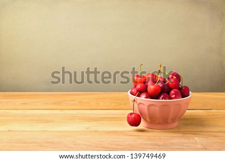 Bowl full of cherries on wooden table over grunge background