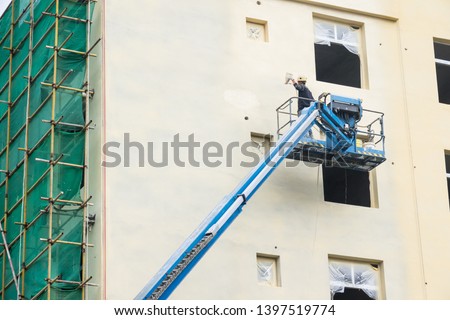A man work painting buliding  by airbrush on crane in construction site