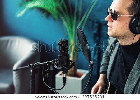 Close up of a man singer sitting on a stool in a headphones with a guitar recording a track in a home studio