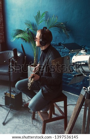 Man singer sitting on a stool in a headphones with a guitar recording a track in a home studio