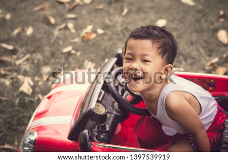 Little boy driving red car with the steering wheel. Little boy driving big toy car and having fun on grass outdoors.