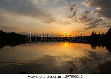 Fantastic bright sunset sky above the water surface. Perfect symmetrical reflection. Black silhouette of forest 