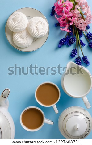Latte, white meringues, milk jar on pastel blue background decorated with muscari and hyacinth flowers. Top down, flat lay. Breakfast and coffee time concept. Copy space. Frame composition. Vertical