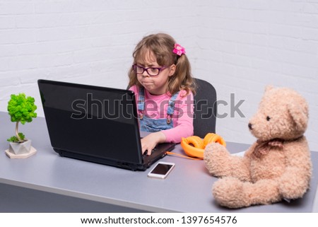 Little girl in glasses with a laptop. A girl playing a video game on a laptop. Schoolgirl doing homework on a laptop.